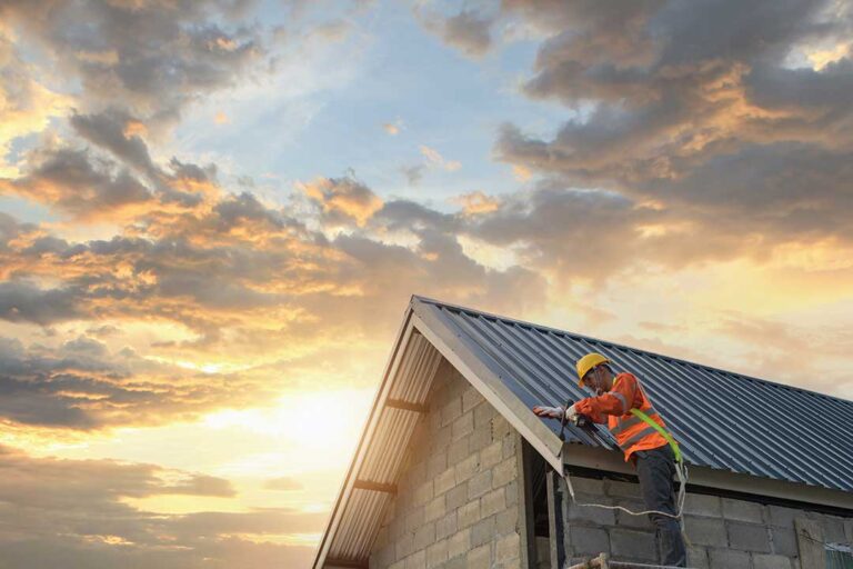 A person examines curling and cracked asphalt shingles on a residential rooftop.