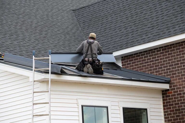 Close view of bruised asphalt shingles with missing granules beside dented metal roof flashing.